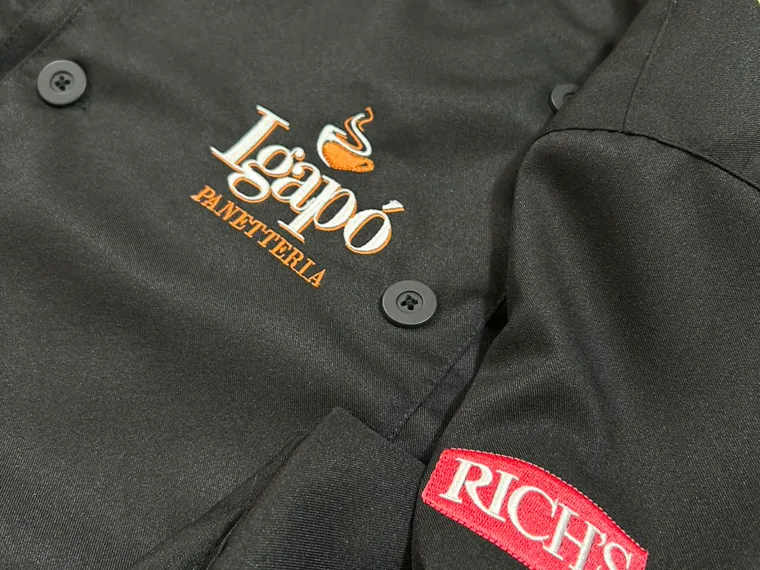 Camisa preta de panetteria produzida pela Ruvest Uniformes, com o bordado da marca no peito e etiqueta na manga